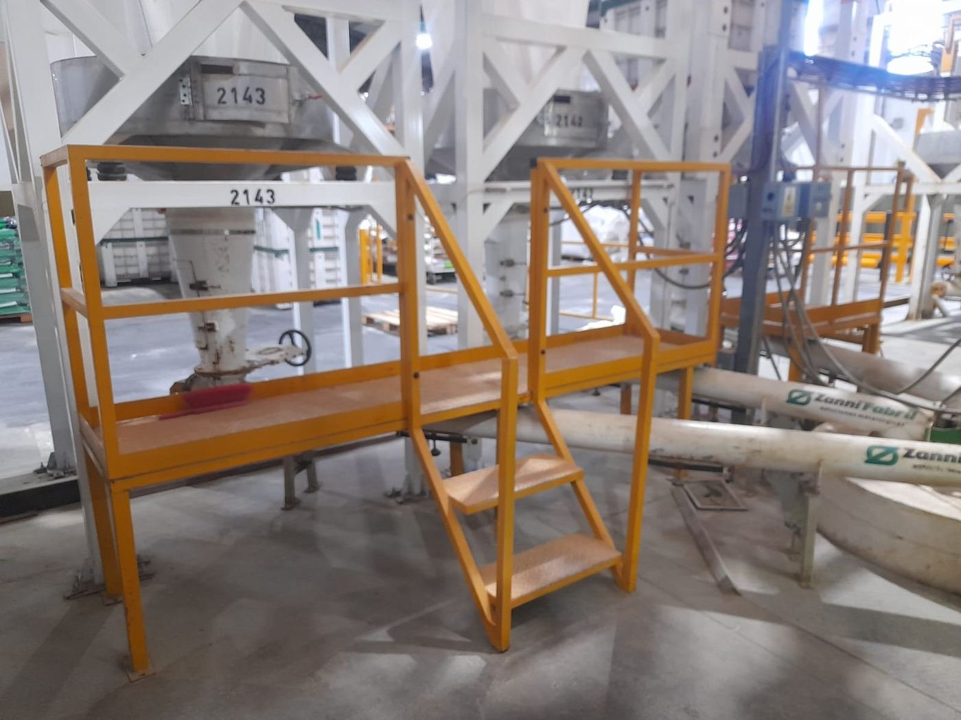 Plataforma de acceso metálica con escalera montada junto a una línea de tolvas